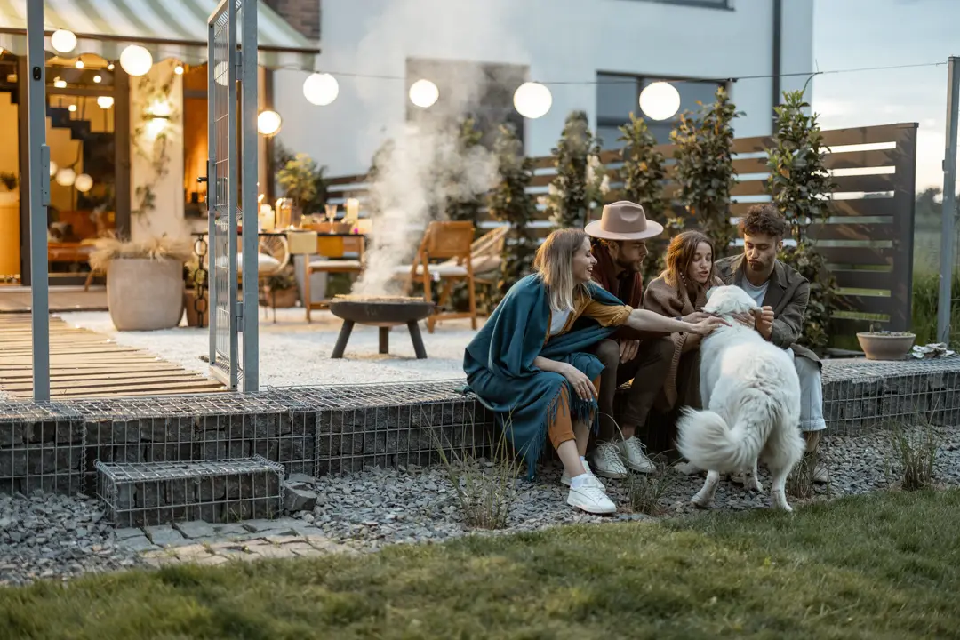 Friends gathered around a fire pit on the back patio of a vacation rental at dusk.